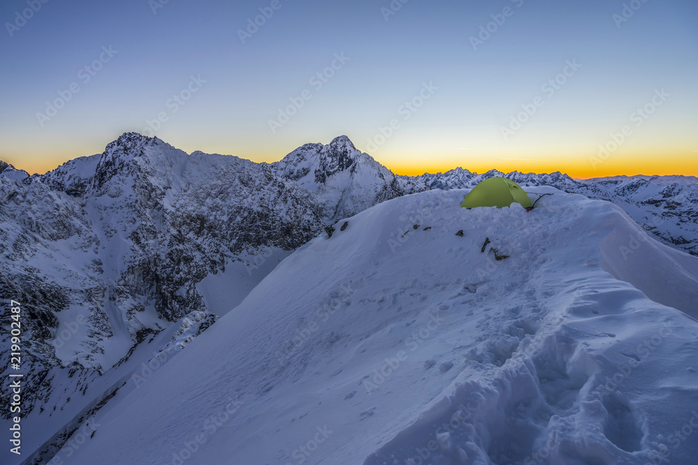 黄色帐篷搭在高山山顶上。冬天在白雪覆盖的山上露营。