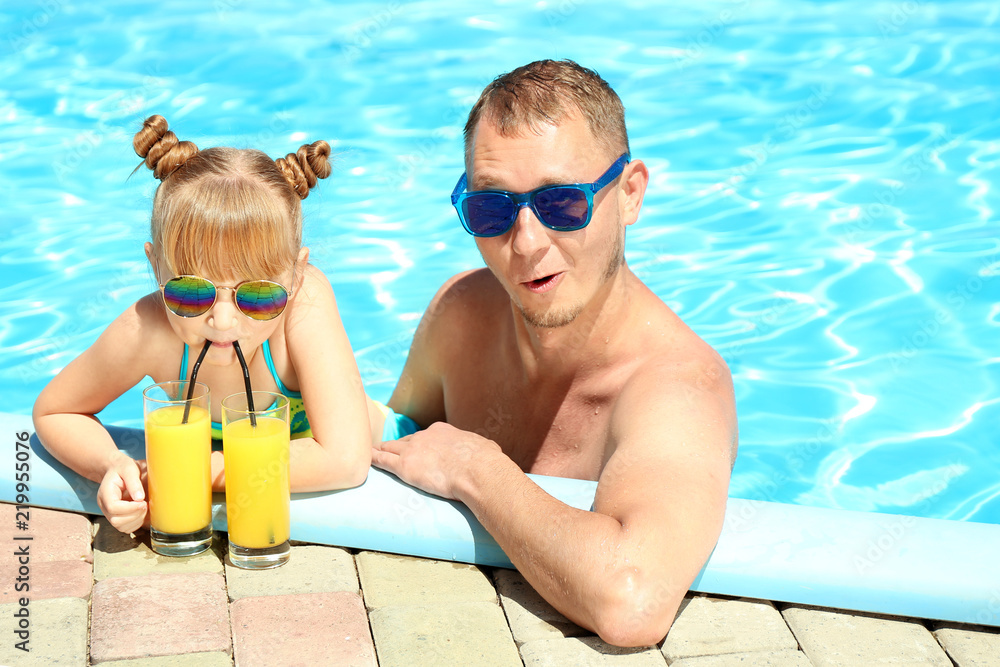 Happy father and daughter with glasses of juice resting in swimming pool