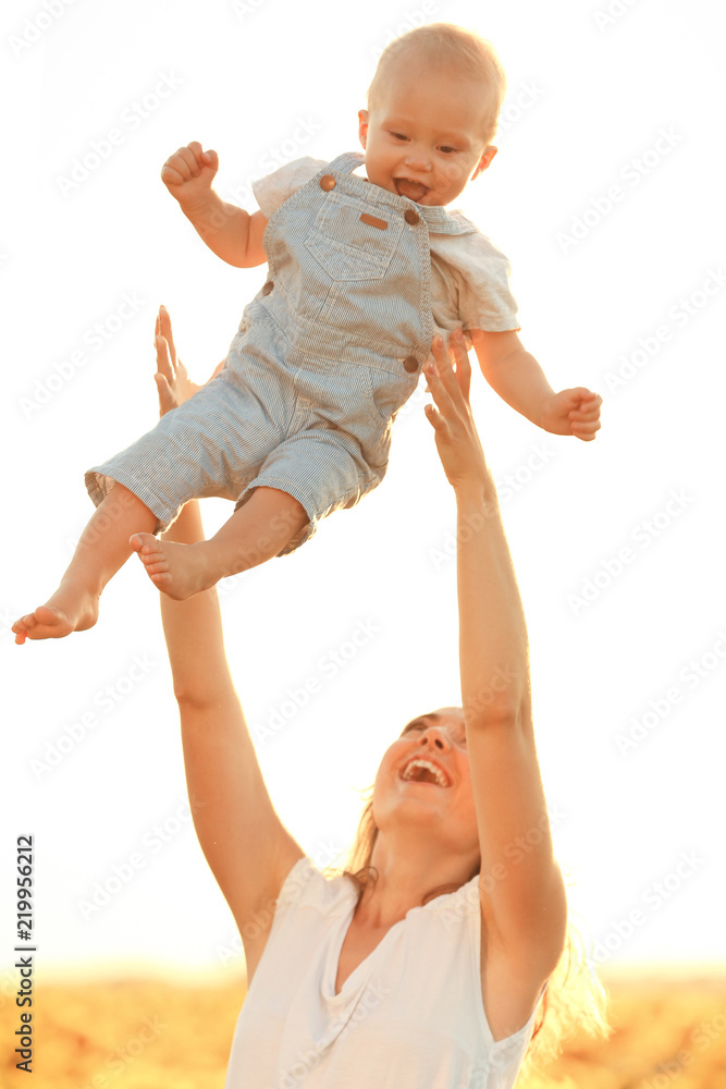 Beautiful woman playing with her little son in sunflower field on summer day