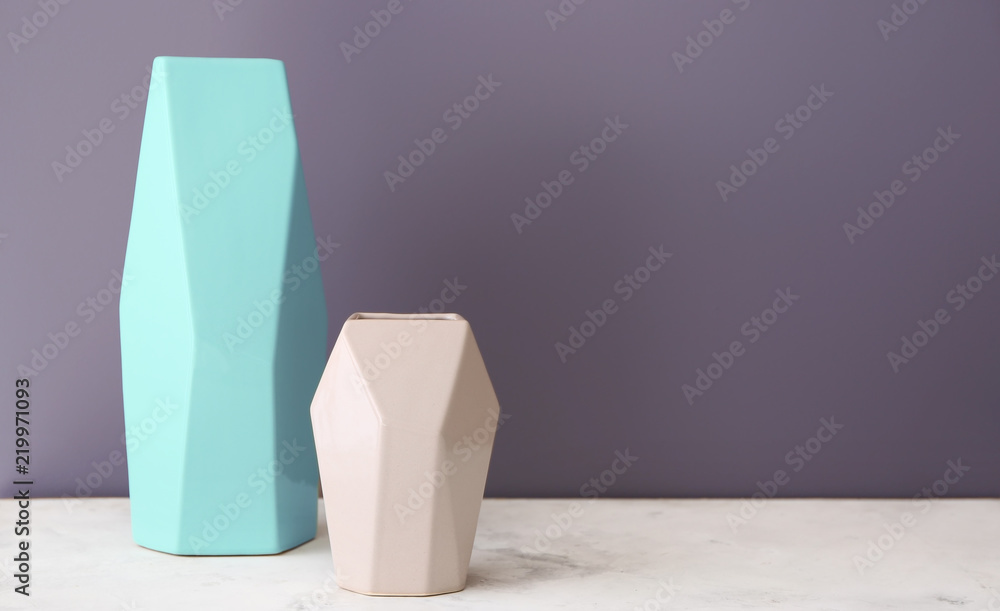 Ceramic vases on table against color background