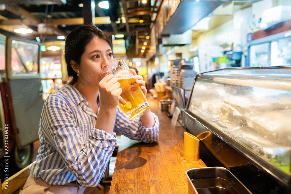 asian woman drinking at the counter of izakaya.