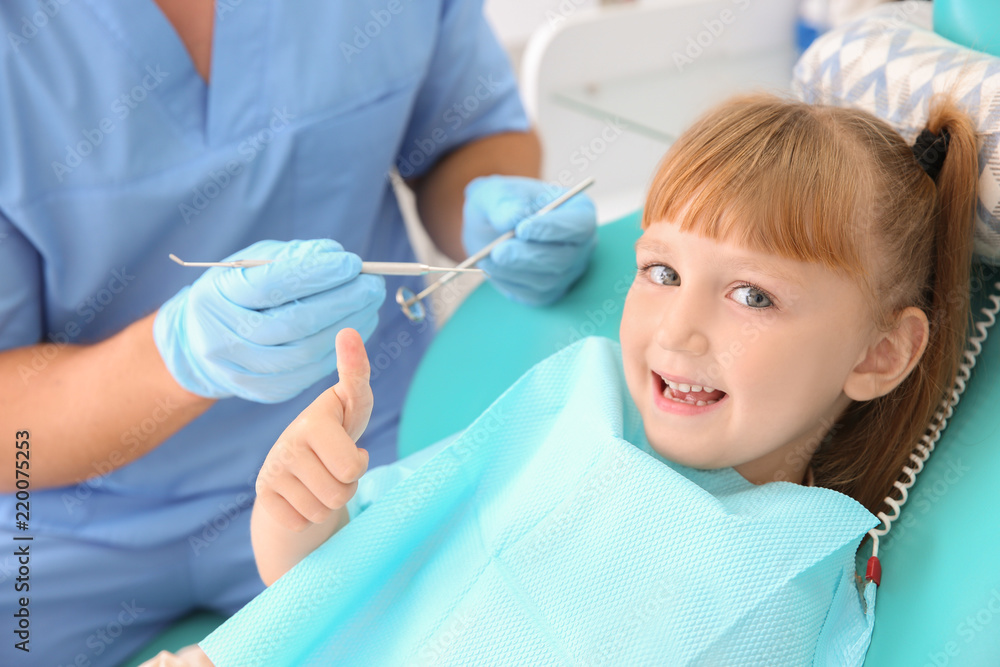 Cute little girl showing thumb-up gesture at dentists office