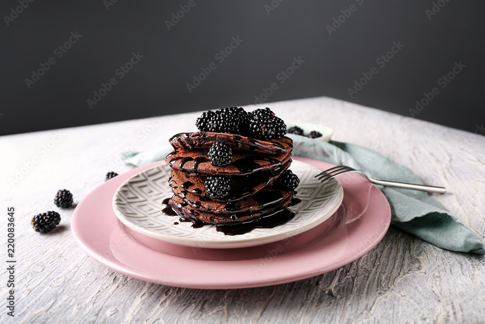 Plate with tasty chocolate pancakes and berries on light wooden table