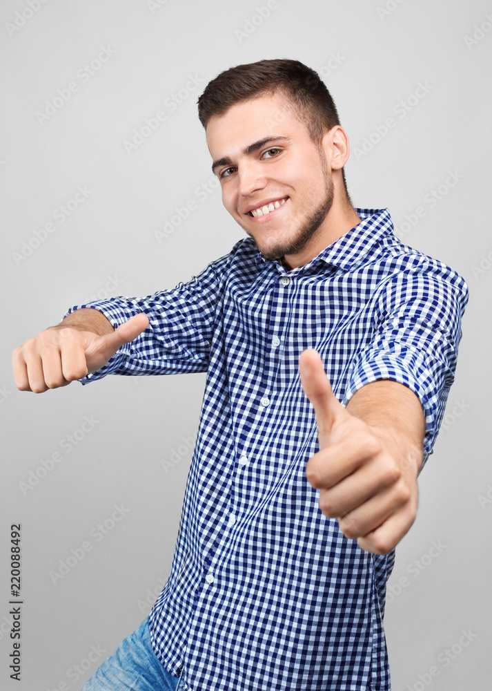 Handsome young man showing thumb-ups gesture on light background