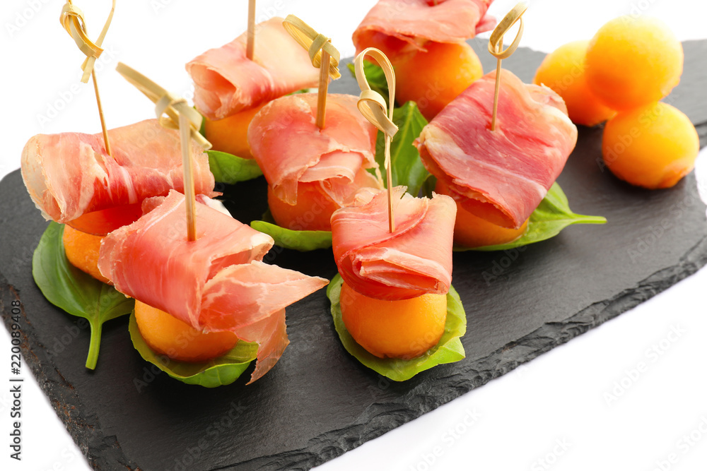 Slate plate with delicious melon balls and prosciutto on white background