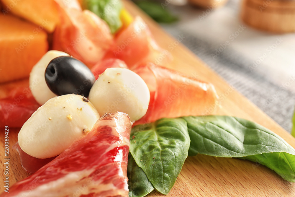 Delicious melon with prosciutto, mozzarella cheese and olives on wooden board, closeup