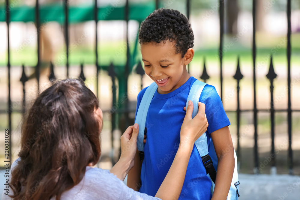 Mother helping her son to put on backpack outdoors