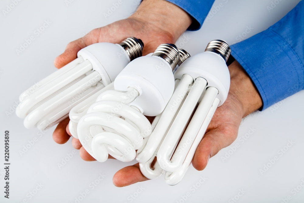 Mans Hands Holding Three Energy Efficient Bulb on Grey（男子手持三个灰色节能灯泡）