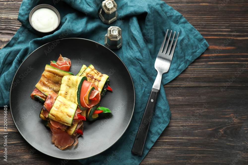 Plate with tasty zucchini rolls on wooden table