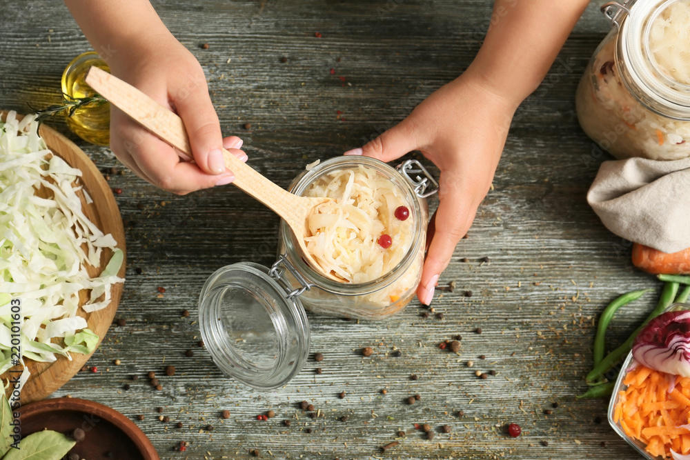 Woman putting homemade sauerkraut into glass jar on table