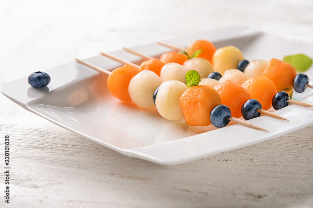 Plate with tasty melon balls on light wooden table