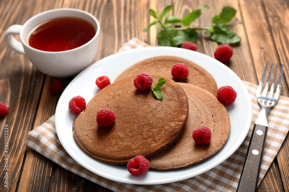 木桌上摆着美味的巧克力煎饼、覆盆子和一杯茶