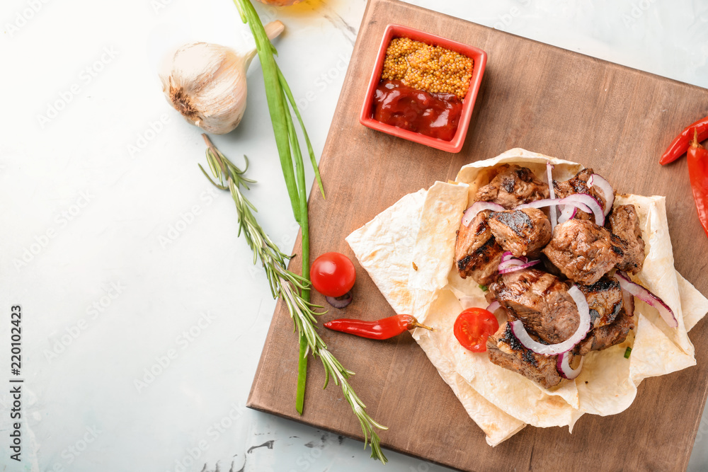 Board with delicious shish kebab and sauce on light table