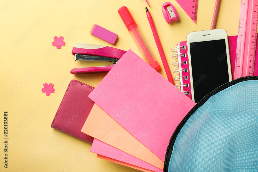 Backpack with school stationery and mobile phone on color background