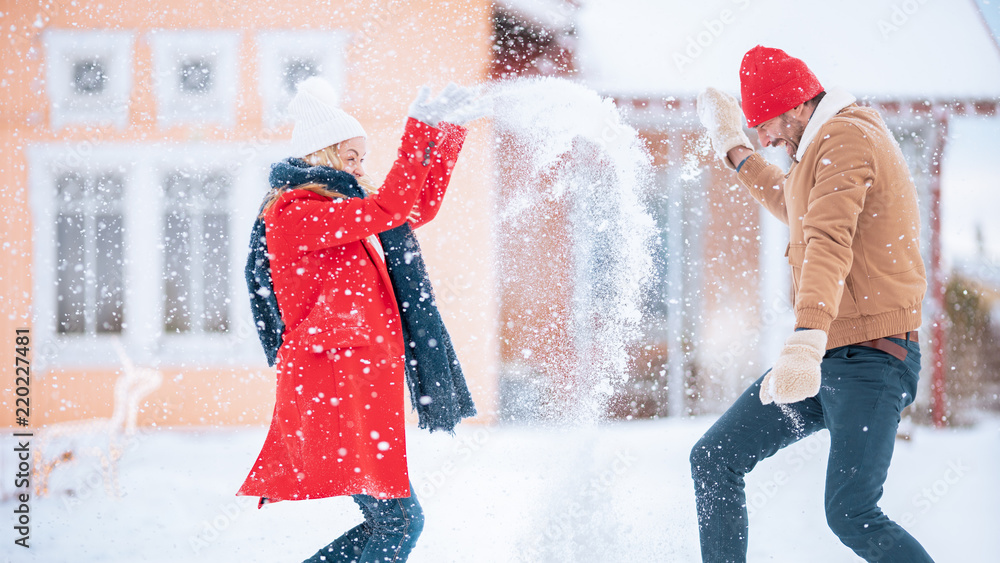 一对年轻夫妇顽皮地把雪抛向空中，而冬天的雪还在继续。快乐的男人和女人