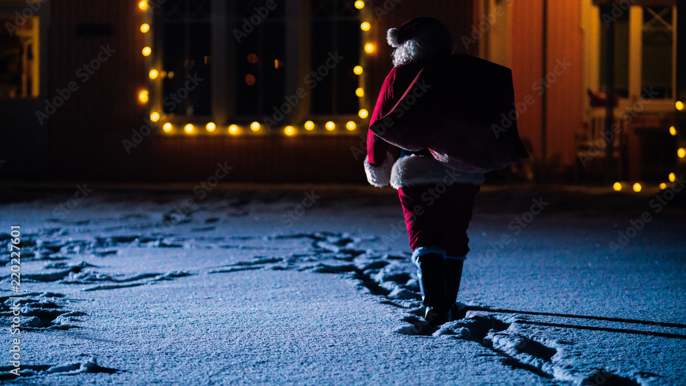 Shot of Santa Claus with Red Bag, Walks into Front Yard of the Idyllic House Decorated with Lights a