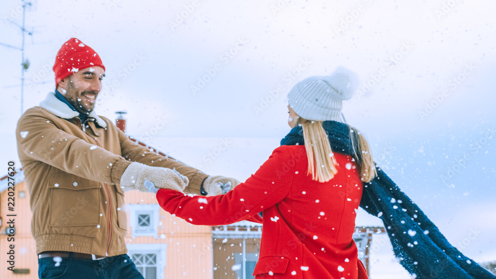 年轻漂亮的情侣在落雪中跳舞和旋转。快乐的男人和女人在院子里玩得开心