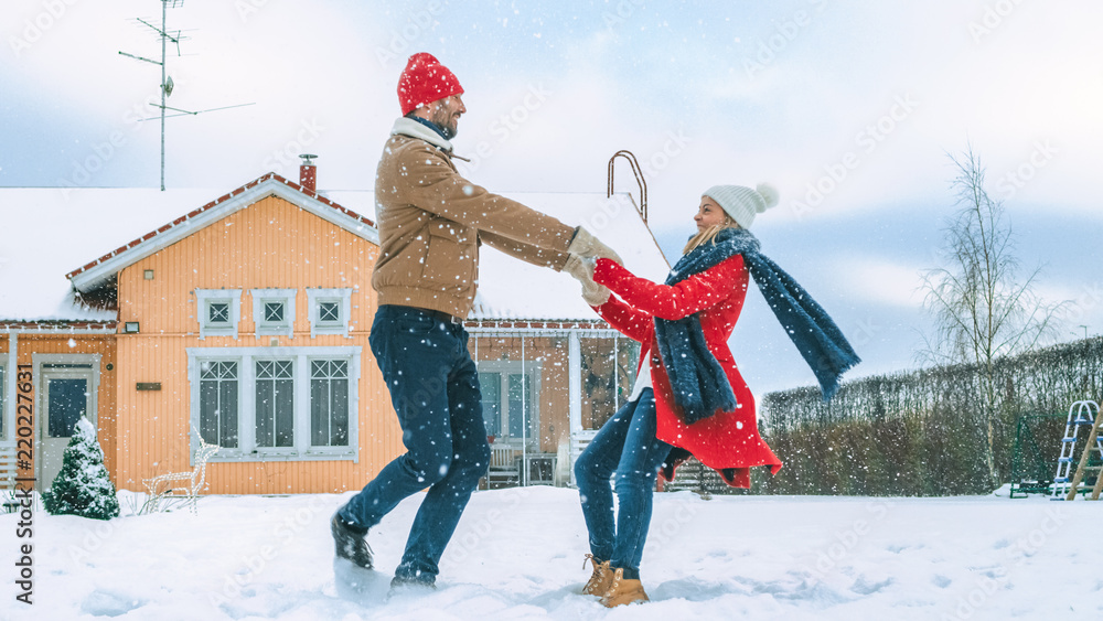 Young Beautiful Couple Dance and Spin in the Falling Snow. Happy Man and Woman Having Fun in the Yar