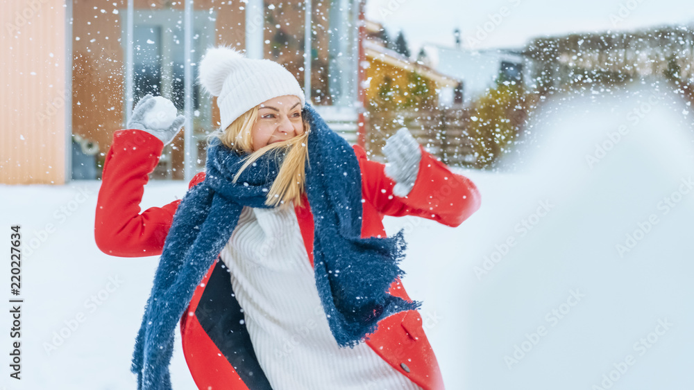 快乐的微笑的年轻女人扔雪球。穿着红色外套的女孩享受冬天。在后院的日子