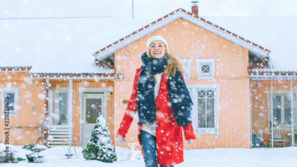 一位身穿红色外套、头戴围巾的年轻金发女子在雪地里走在后院的肖像