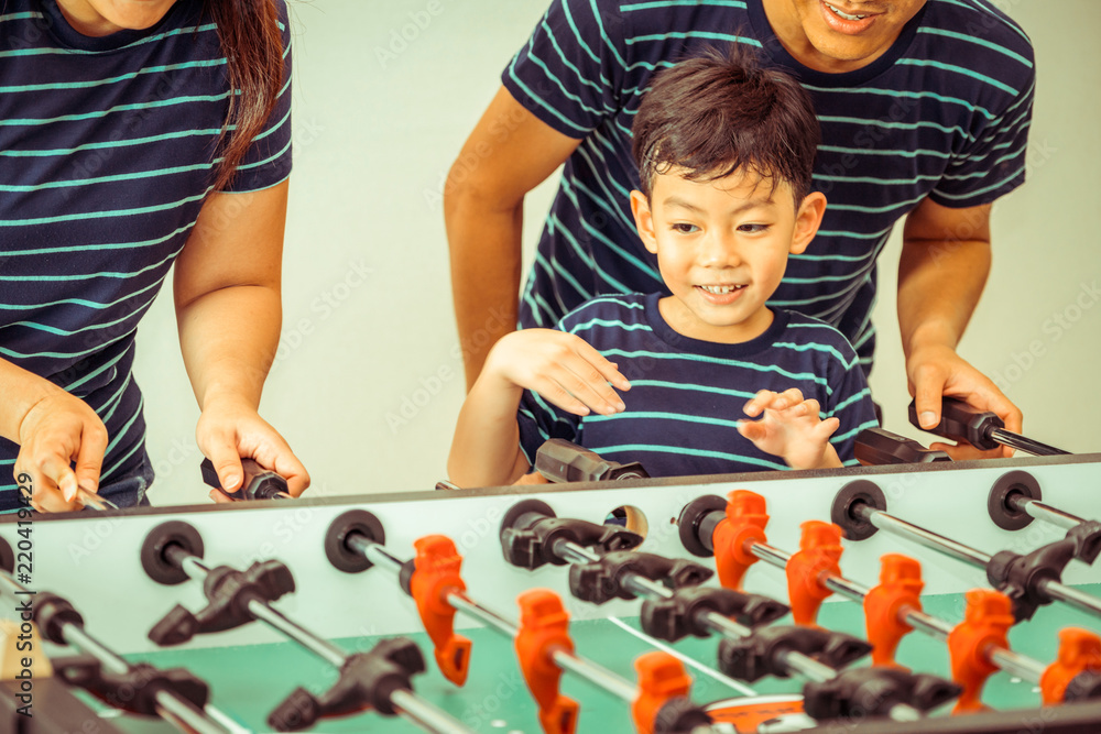 Happy kid playing foosball table with family.