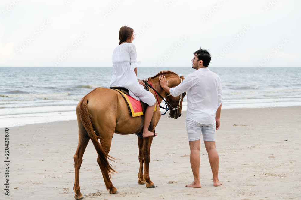 一对年轻夫妇在热带海滩上骑马。