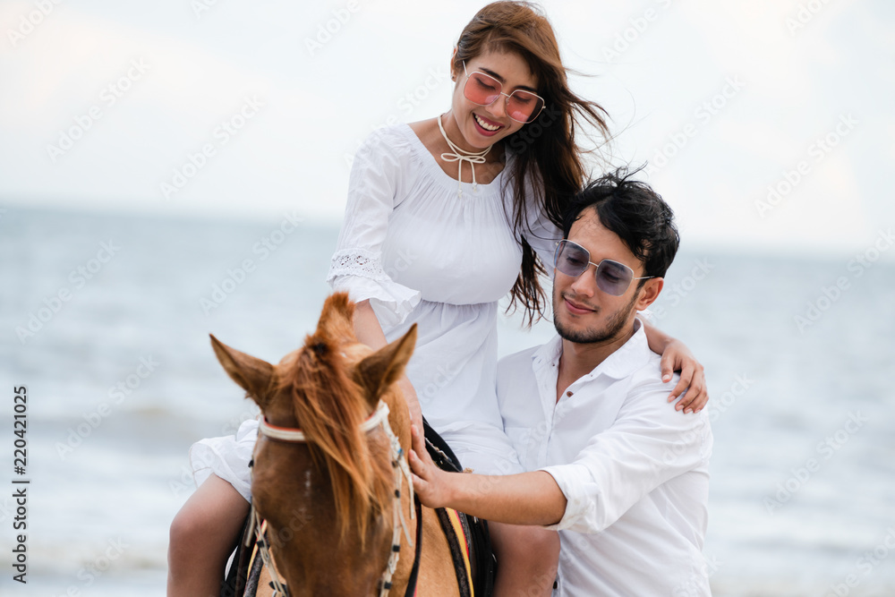 Young couple goes horse riding on tropical beach.