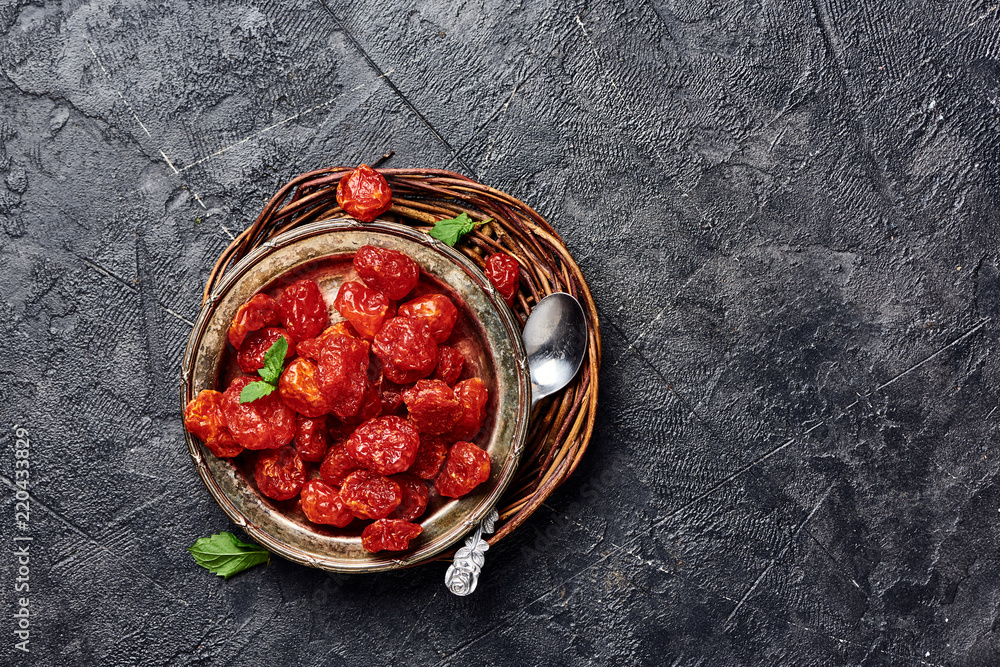 Candied cherry tomatoes on black background. Top view of dessert.