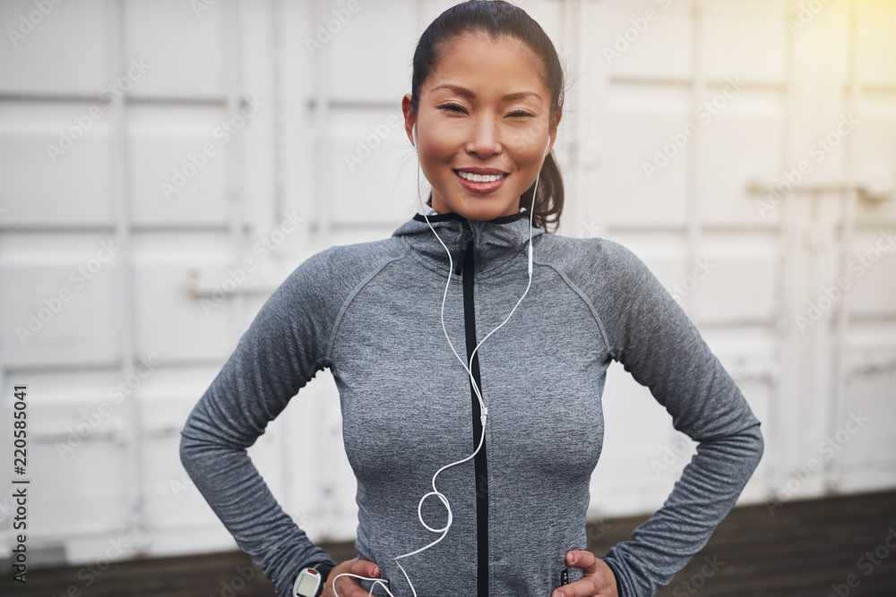 Smiling young Asian woman standing outdoors ready for a run