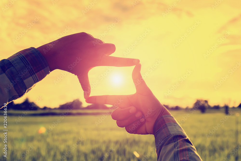 looking hand frame distant view with sunrise over field