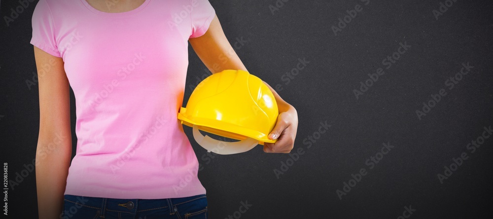 Composite image of woman holding hard hat against grey