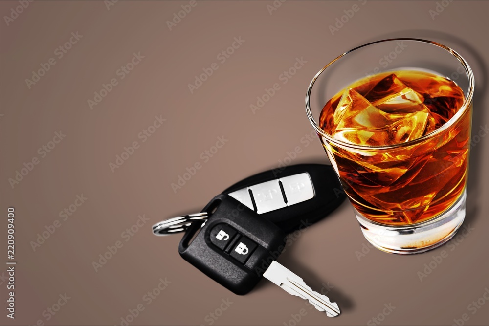 Glass of whiskey and car key on wooden background