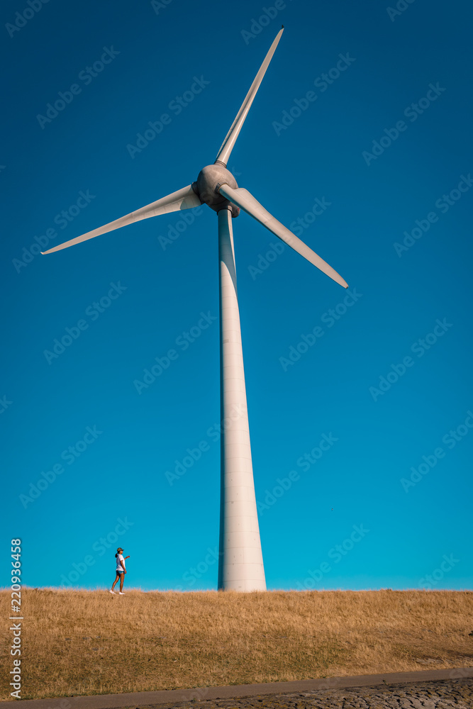 young woman pointing finger to an huge windmill by the dike at the lake ijsselmeer Netherlands, huge