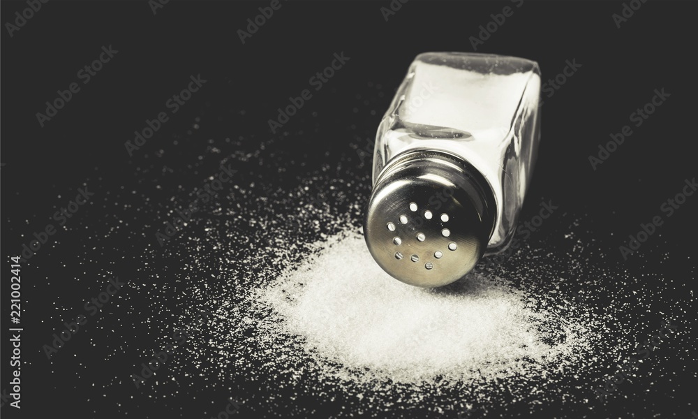 Female hand pouring salt from salt shaker on black background