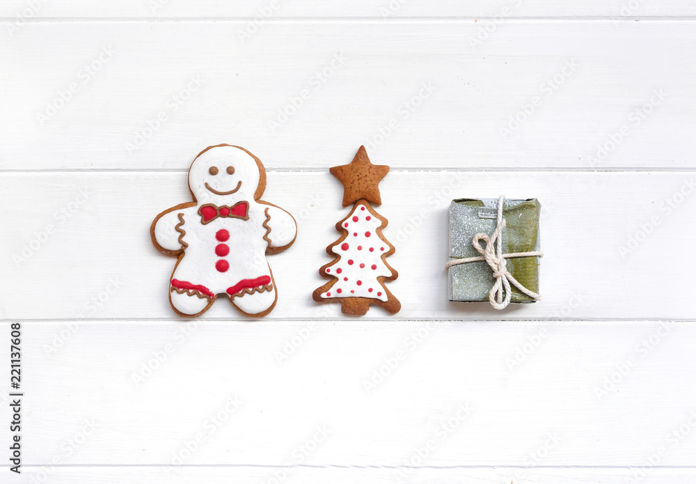 Сreative Christmas composition with glazed gingerbread men, Christmas tree and gift on white wooden 