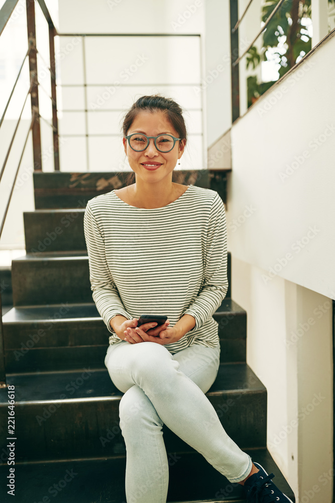 微笑的年轻亚洲女商人坐在楼梯上举着ce