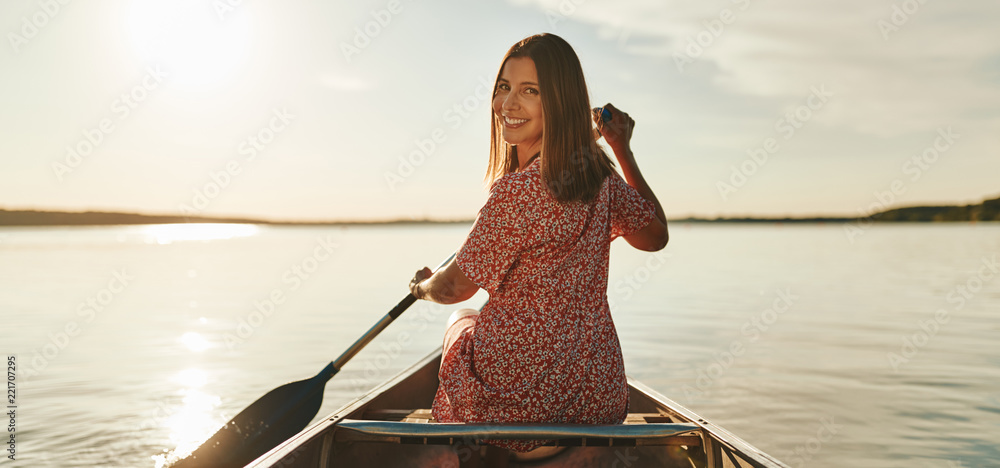 微笑的年轻女子夏天在平静的湖面上划独木舟