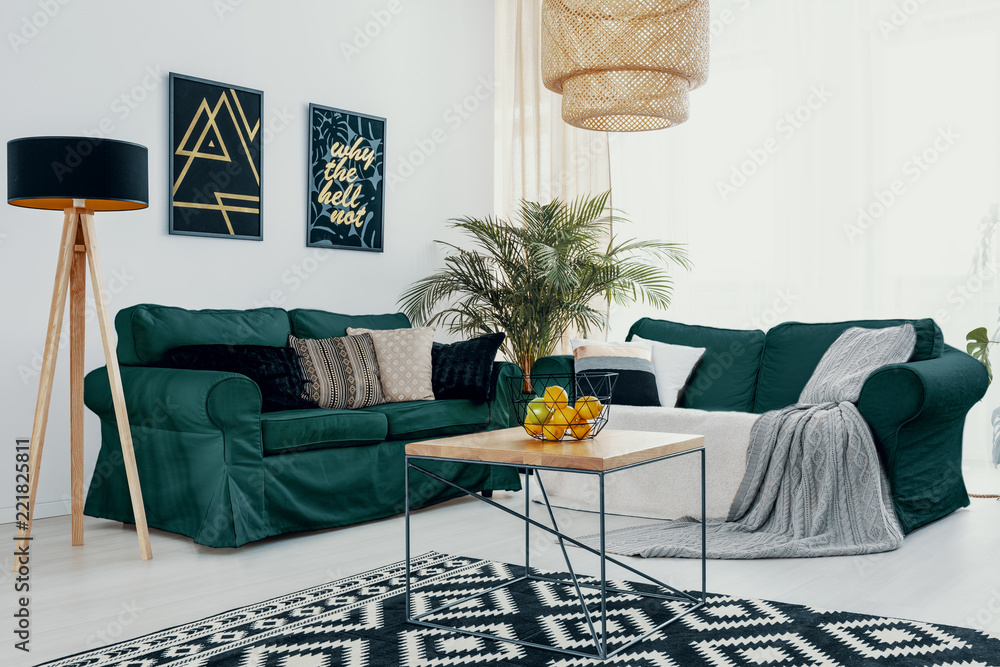 Wooden table in front of green sofa in white living room interior with lamp and posters. Real photo