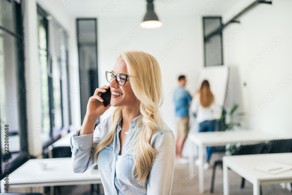 Young business woman having a phone call. Colleagues in the background, working on white board.