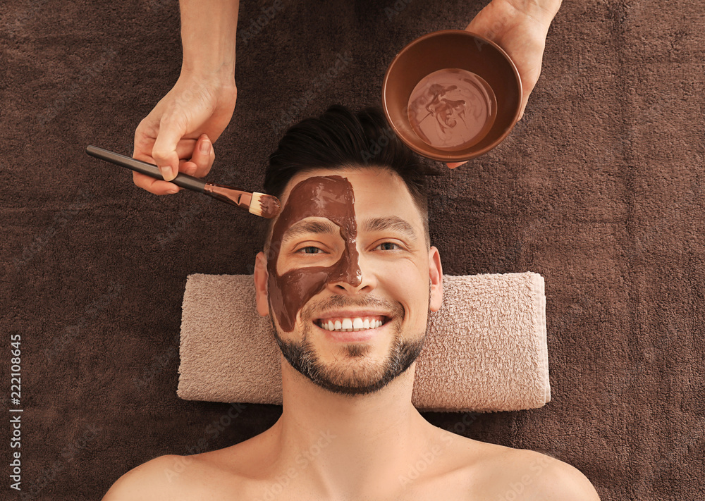 Beautician applying cosmetic mask on mans face in spa salon