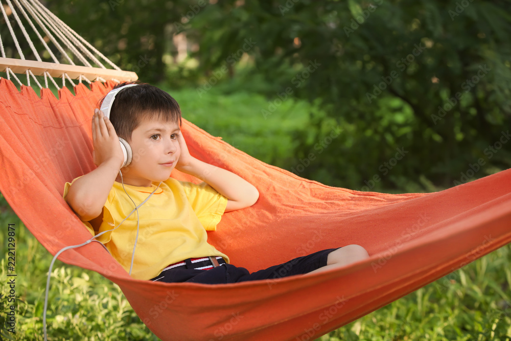 Cute little boy listening to music while relaxing in hammock on summer day