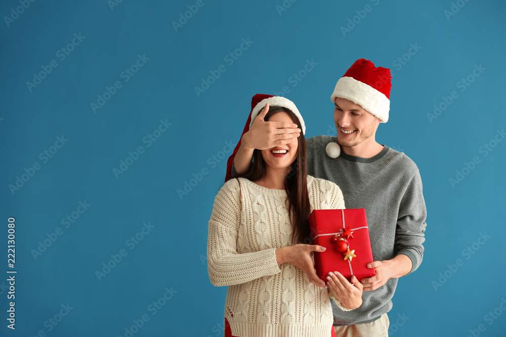 Young woman receiving Christmas gift from her husband on color background