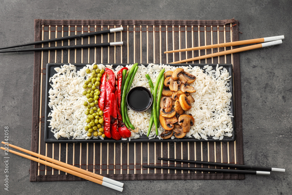 Plate with tasty boiled rice and vegetables on grey table