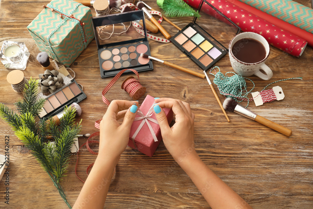 Woman with Christmas present and set of decorative cosmetics on wooden background