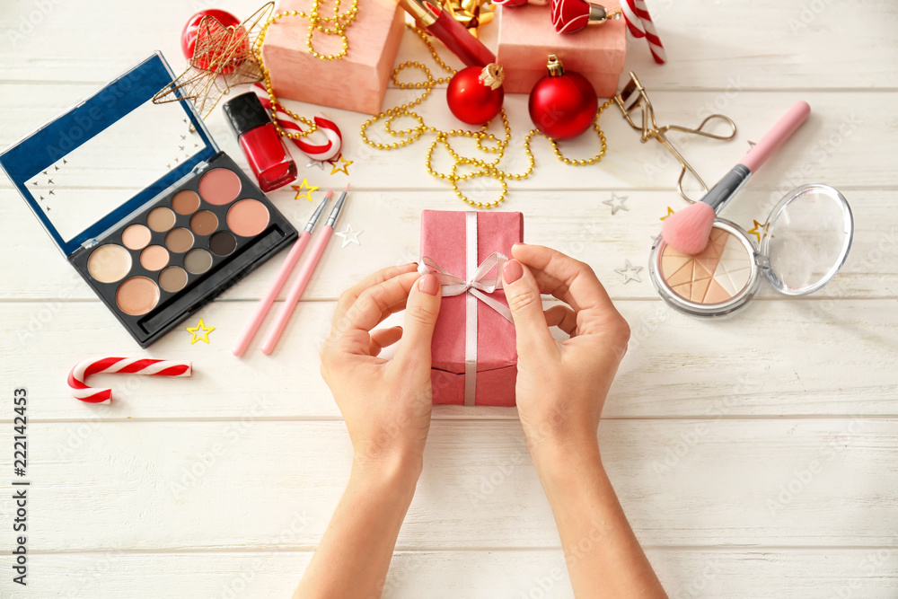 Woman with Christmas present and set of decorative cosmetics on white wooden background