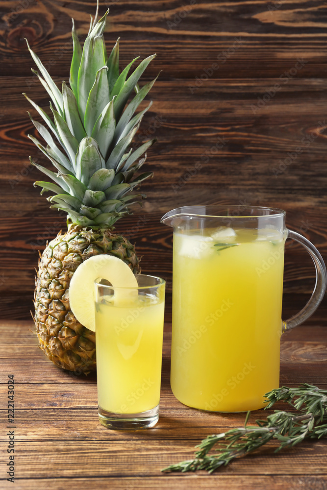 Glass and jug with tasty fresh pineapple drink on wooden table