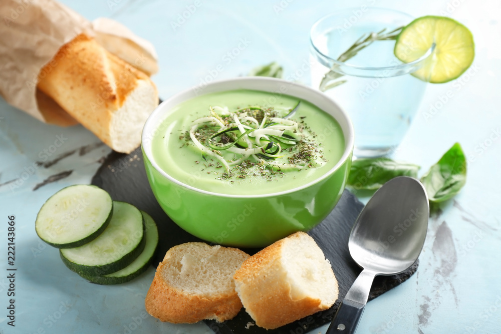 Bowl with delicious zucchini soup and french bread on light table