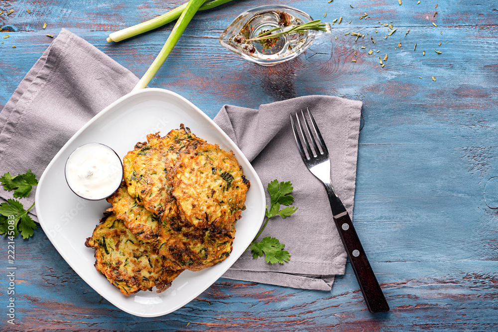 Plate with tasty zucchini pancakes on wooden table