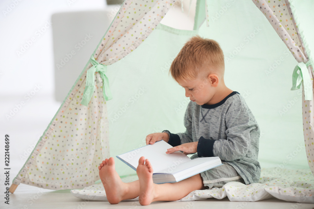 Cute little boy reading book in hovel at home