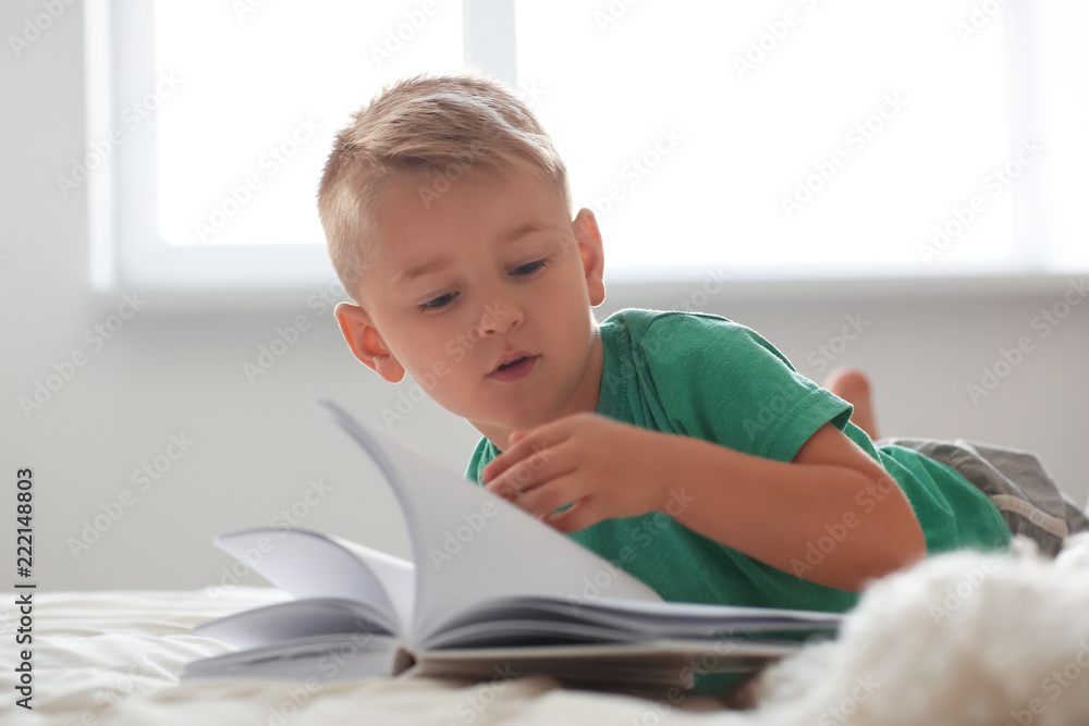 Cute little boy reading book on bed at home